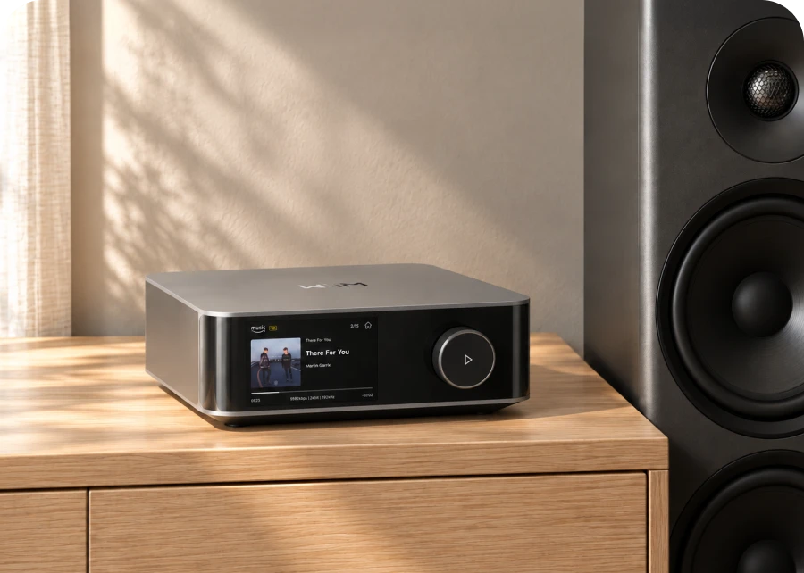 WiiM Amp Ultra on a wooden cabinet next to a large tower speaker
